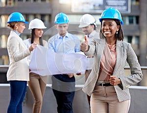 Architects who care. a young female architect showing a thumbs up while working with coworkers against a city background