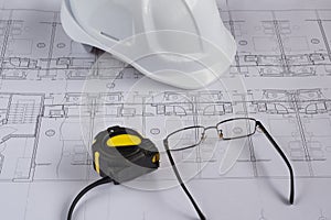 Architects workplace - architectural blueprints with measuring tape, safety helmet and glasses on table. Top view.