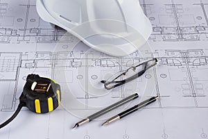 Architects workplace - architectural blueprints with measuring tape, safety helmet and glasses on table. Top view.