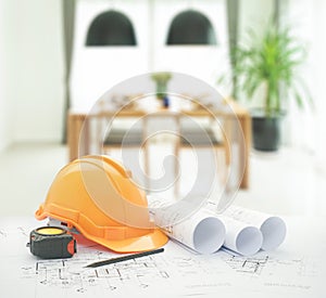 Architectural blueprint with safety helmet and tools over dining table and comfortable chairs