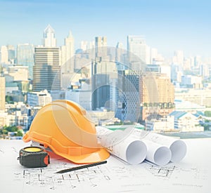 Architectural blueprint with safety helmet and tools over modern business district with high building