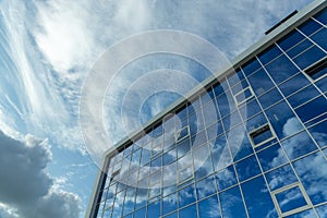 Architectural detail of the facade with multiple reflections of cloudy sky and the sun