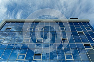 Architectural detail of the facade with multiple reflections of cloudy sky and the sun