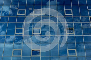 Architectural detail of the facade with multiple reflections of cloudy sky and the sun