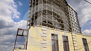 Architectural detail of high frame of monolithic concrete building under construction and old demolished house in front