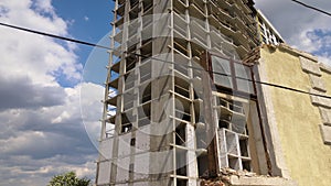 Architectural detail of high frame of monolithic concrete building under construction and old demolished house in front