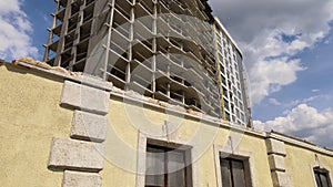 Architectural detail of high frame of monolithic concrete building under construction and old demolished house in front