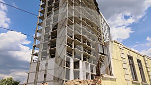 Architectural detail of high frame of monolithic concrete building under construction and old demolished house in front