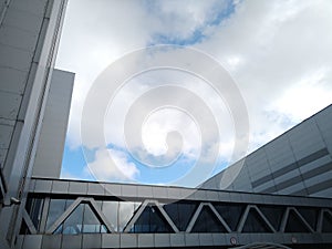 Architecture of a modern industrial and office building with a glass transition between two buildings with blue sky and white clou