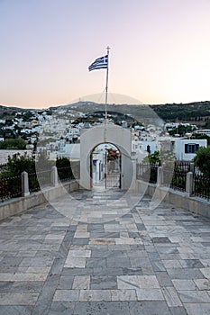 Archway leading to a white city gate adorned with a waving Greek flag