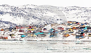 Arctic city center panorama with colorful Inuit houses on the rocky hills covered in snow with snow and mountain in the background