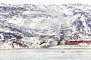 Arctic city panorama with colorful Inuit cottages and oil factory on the rocky hills covered in snow and mountain in the