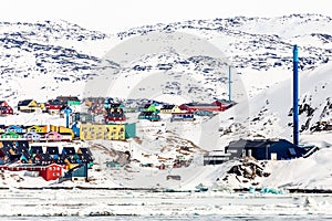 Arctic city panorama with colorful Inuit cottages and powerplant on the rocky hills covered in snow and mountain in the background