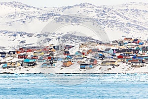 Arctic city panorama with colorful Inuit houses on the rocky hills covered in snow with snow and mountain in