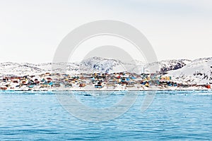 Arctic city panorama with colorful Inuit houses on the rocky hills covered in snow with snow and mountain in