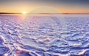 The Arctic cold landscape of icy lake at sunset with textural cracks and patterns on the ice.