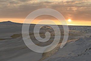Arctic landscape in winter time. Small river with ice in tundra. Sunset