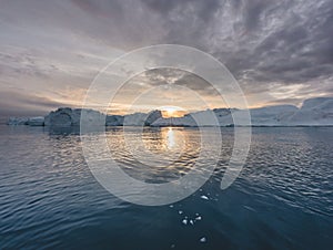 Arctic nature landscape with icebergs in Greenland icefjord with midnight sun sunset sunrise in the horizon. Early
