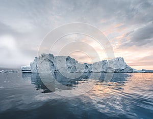 Arctic nature landscape with icebergs in Greenland icefjord with midnight sun sunset sunrise in the horizon. Early