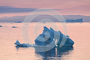 Arctic nature landscape with icebergs in Greenland icefjord with midnight sun sunset / sunrise in the horizon.  Early morning