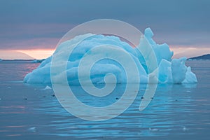 Arctic nature landscape with icebergs in Greenland icefjord with midnight sun sunset / sunrise in the horizon.  Early morning