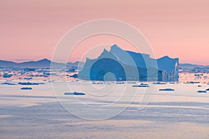 Arctic nature landscape with icebergs in Greenland icefjord with midnight sun sunset / sunrise in the horizon.  Early morning