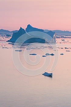 Arctic nature landscape with icebergs in Greenland icefjord with midnight sun sunset / sunrise in the horizon.  Early morning