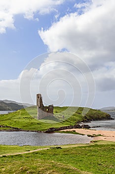 Ardvreck Castle ruins perched on a vibrant green isthmus overlooking a serene lake and gentle hills
