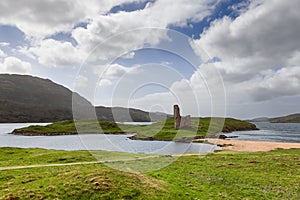 Ardvreck Castle ruins on a strip between lake and sea, framed by hills, under a dynamic sky