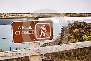 Area Closed sign posted on the Pacific Ocean coast in Marin Headlands, Marin County; Golden Gate Bridge engulfed by fog visible in