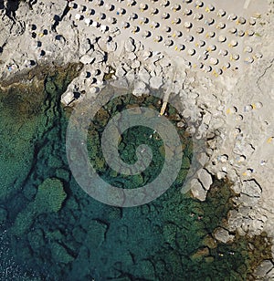 Areal view on a rocky beach and turquoise sea with sunbeds and parasols