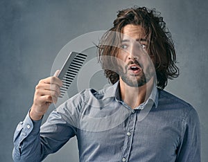 Arent you suppose to fix the mess on my head. a handsome young man looking at the comb after combing his hair.