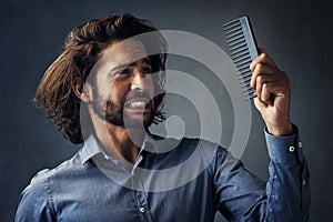 Arent you suppose to fix the mess on my head. Studio shot of a handsome young man looking at his comb while brushing his