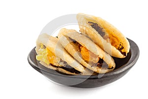 Arepa de huevo. Traditional Colombian fried arepa filled with egg and shredded meat served in a black ceramic dish on white
