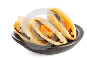 Arepa de huevo. Traditional Colombian fried arepa filled with egg and shredded meat served in a black ceramic dish on white