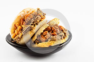 Arepas filled with shredded beef and pork rind served in a black ceramic dish