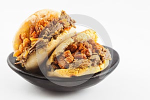 Arepas filled with shredded beef and pork rind served in a black ceramic dish photo