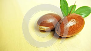 Argan nuts with green leaves motion on wooden background.