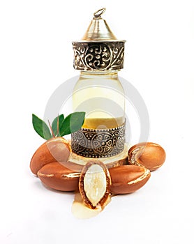 Argan oil in a oriental glass and metal bottle and argan nuts with green leaves isolated on white background.