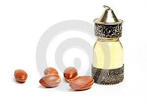 Argan oil in a oriental glass and metal bottle and argan nuts with green leaves isolated on white background.