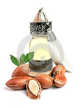 Argan oil in a oriental glass and metal bottle and argan nuts with green leaves isolated on white background.