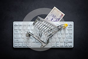 Argentinian money, White computer keyboard, Miniature shopping cart, Black background, Online shopping concept in stores, Low