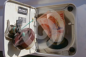 Argentinian pesos fitted into a fuel filler or gas hole of a car\'s fuel tank.