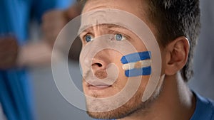 Argentinian soccer fan watching football game on tv, hope of victory, closeup