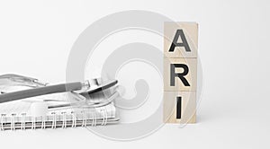 ari inscription on wooden cubes isolated on white background, medicine concept. Nearby on the table are a stethoscope and pills