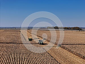 Arial view of combine harvesting a corn field with a tractor and grain cart