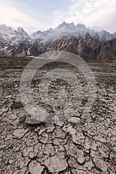 Arid climate, dry cracked drought field with Passu Cathedral mountain landscape in Pakistan