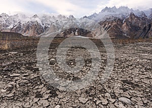 Arid climate, dry cracked drought field with Passu Cathedral mountain landscape in Pakistan