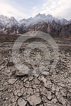 Arid climate, dry cracked drought field with Passu Cathedral mountain landscape in Pakistan photo