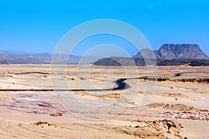 An arid hot desert with mountains and a road under a blue sky